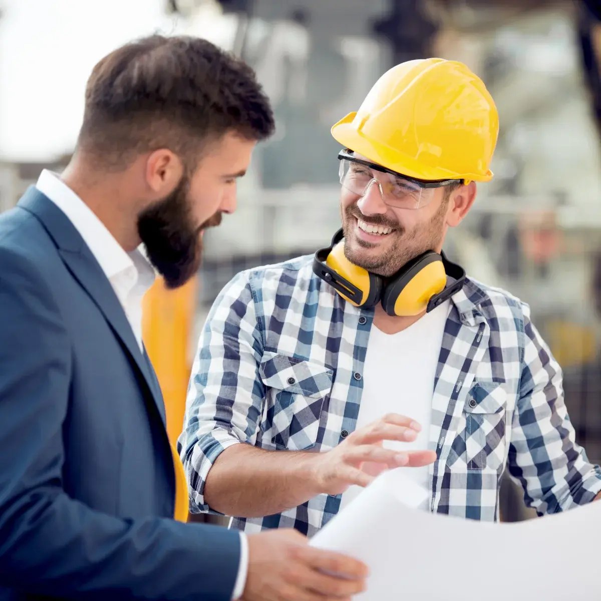 Two professionals reviewing HVAC project plans onsite — one in a hard hat and PPE, the other in business attire — representing Air Theory’s flexible, stage-based ventilation consulting and Catch-Up Kits for passive house and mechanical services projects.