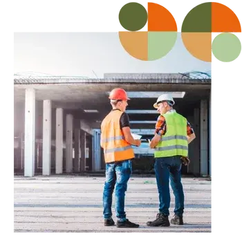 Two facility managers in hard hats and safety vests stand inside a large industrial warehouse, inspecting the space and discussing operations. Represents Air Theory’s support for facility managers and operators with efficient, maintainable, standards-documented mechanical systems.